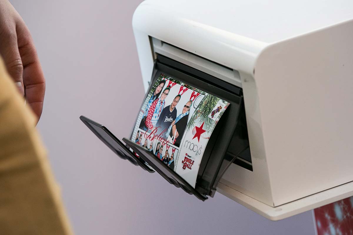 A 4x6 photo booth print is shown coming out of the printer