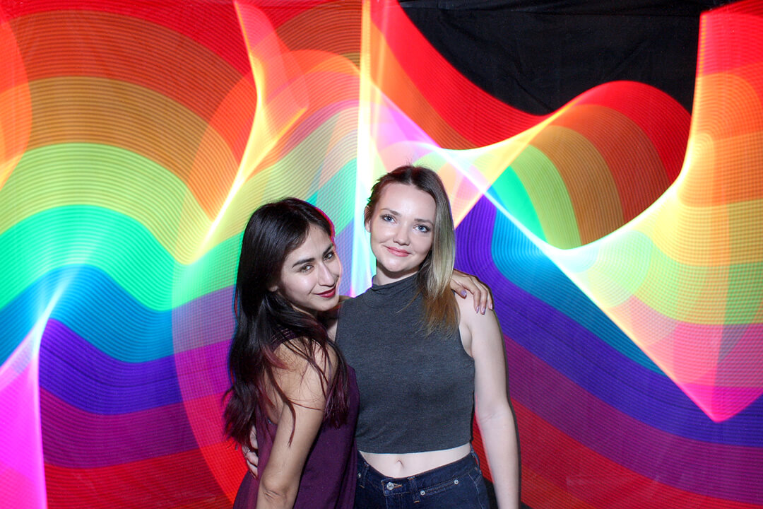 photo booth image of two friends posing while a background is created with light painting