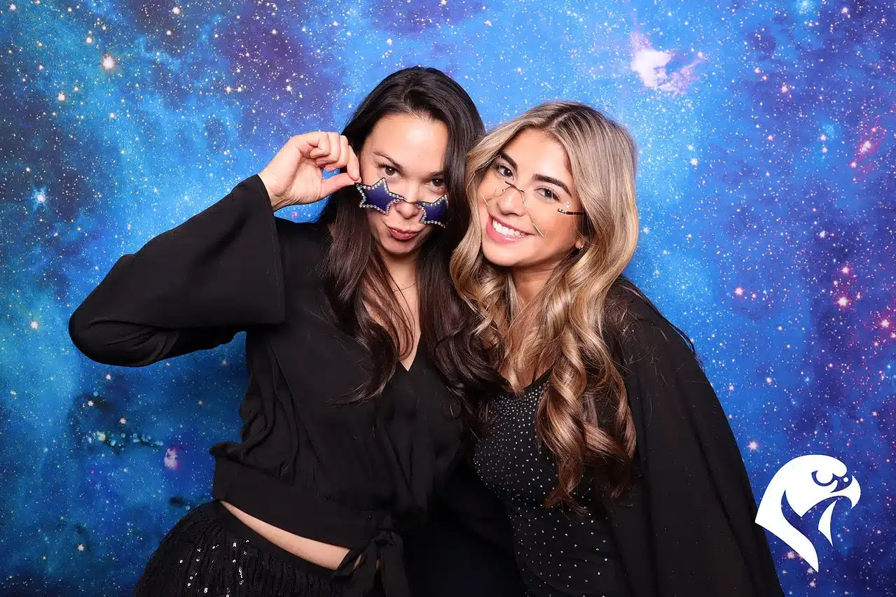 Two women smiling and posing in front of a celestial-themed backdrop at Keopix photo booth during the Celestial Soirée event