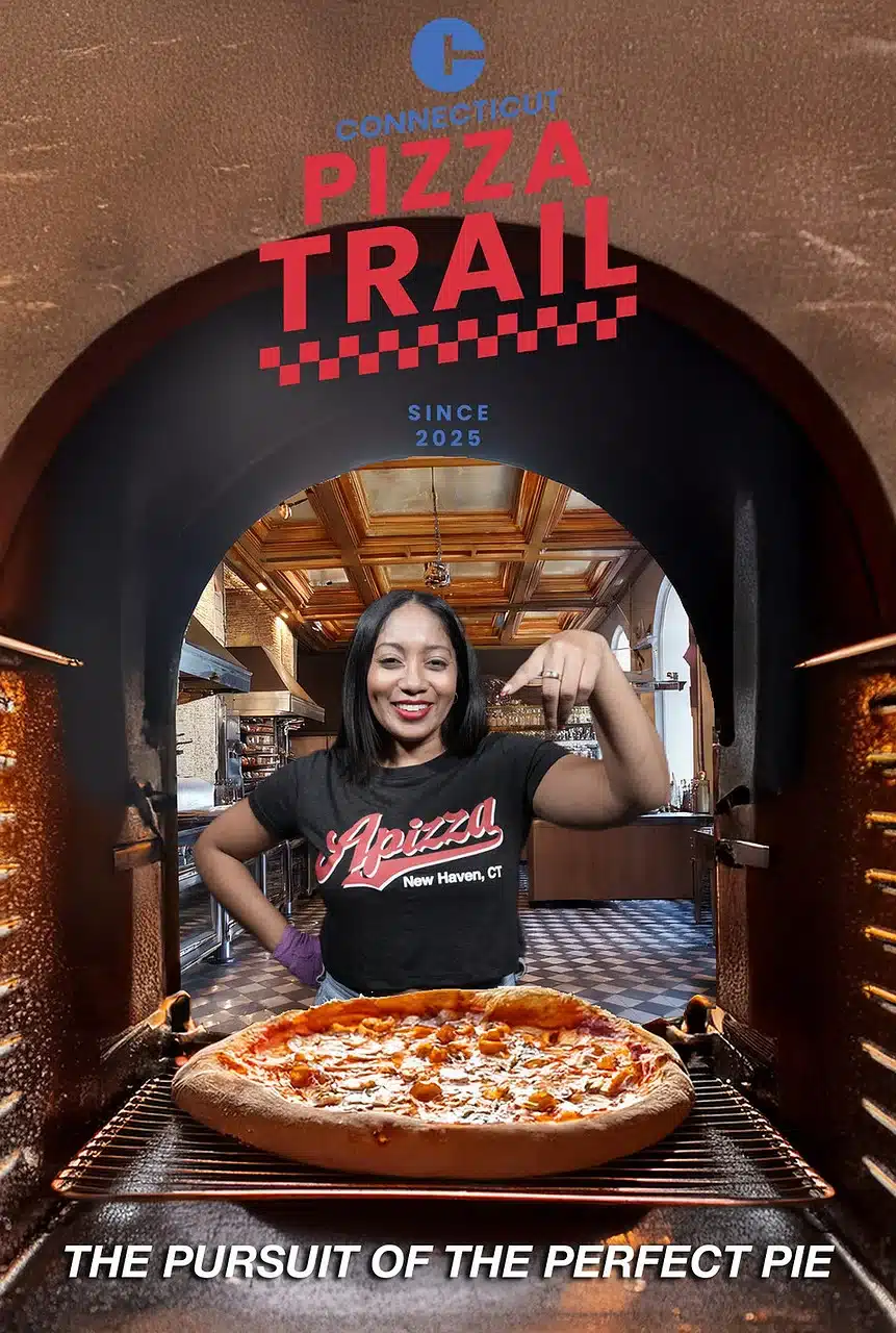 Woman flexing in front of pizza oven during Connecticut Pizza Trail event, wearing an Apizza New Haven shirt