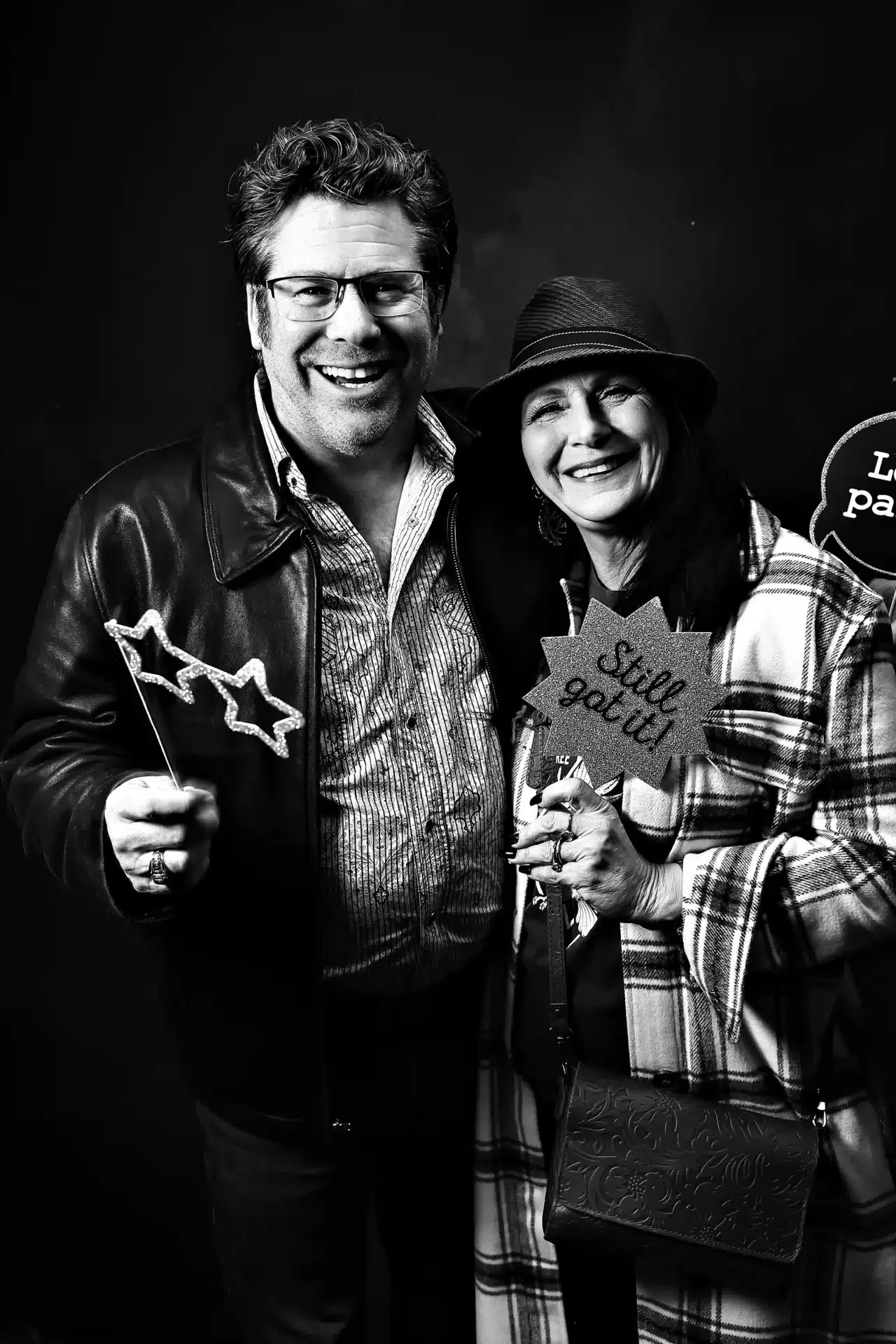Two smiling guests holding photo booth props in a black and white portrait during Keopix activation
